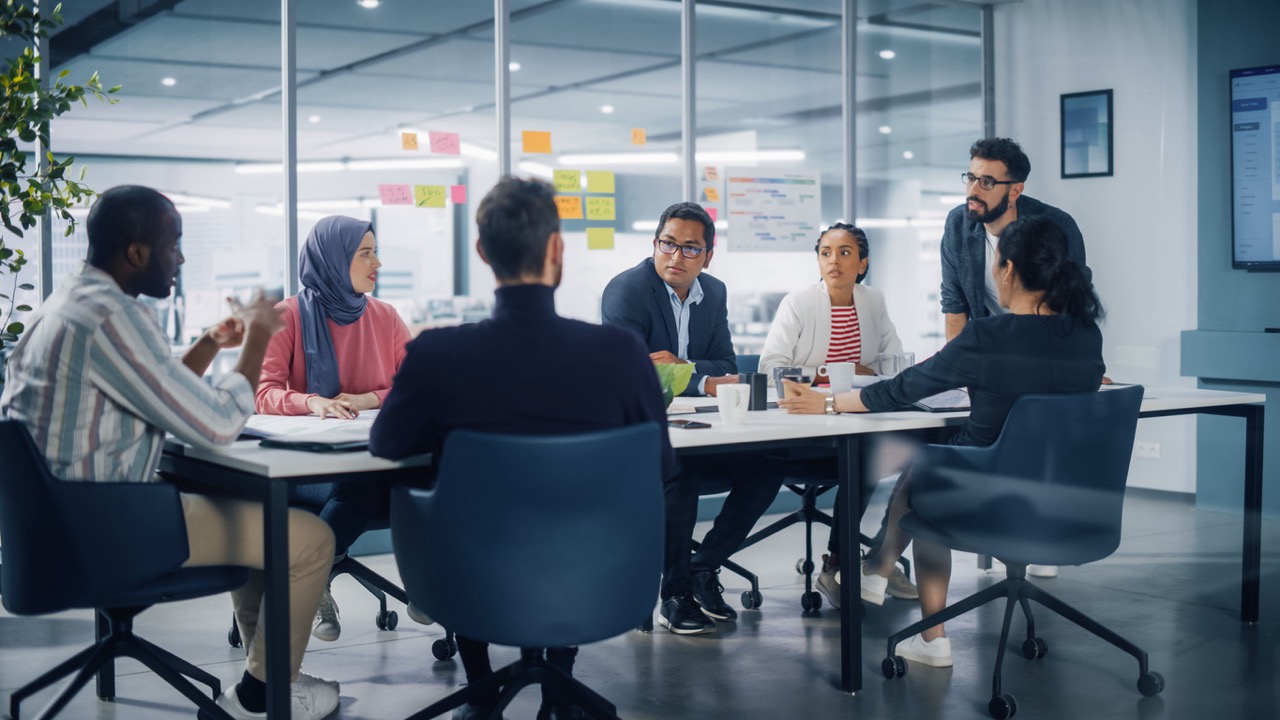 اجتماع في غرفة اجتماعات مكتبية متعددة الأعراق، فريق متنوع من المتخصصين في رواد الأعمال الشباب يتحدثون ويستخدمون التلفزيون للرسوم البيانية التوضيحية، رجال أعمال مبتسمون يناقشون استراتيجية الاستثمار في شركة ناشئة في مجال التجارة الإلكترونية